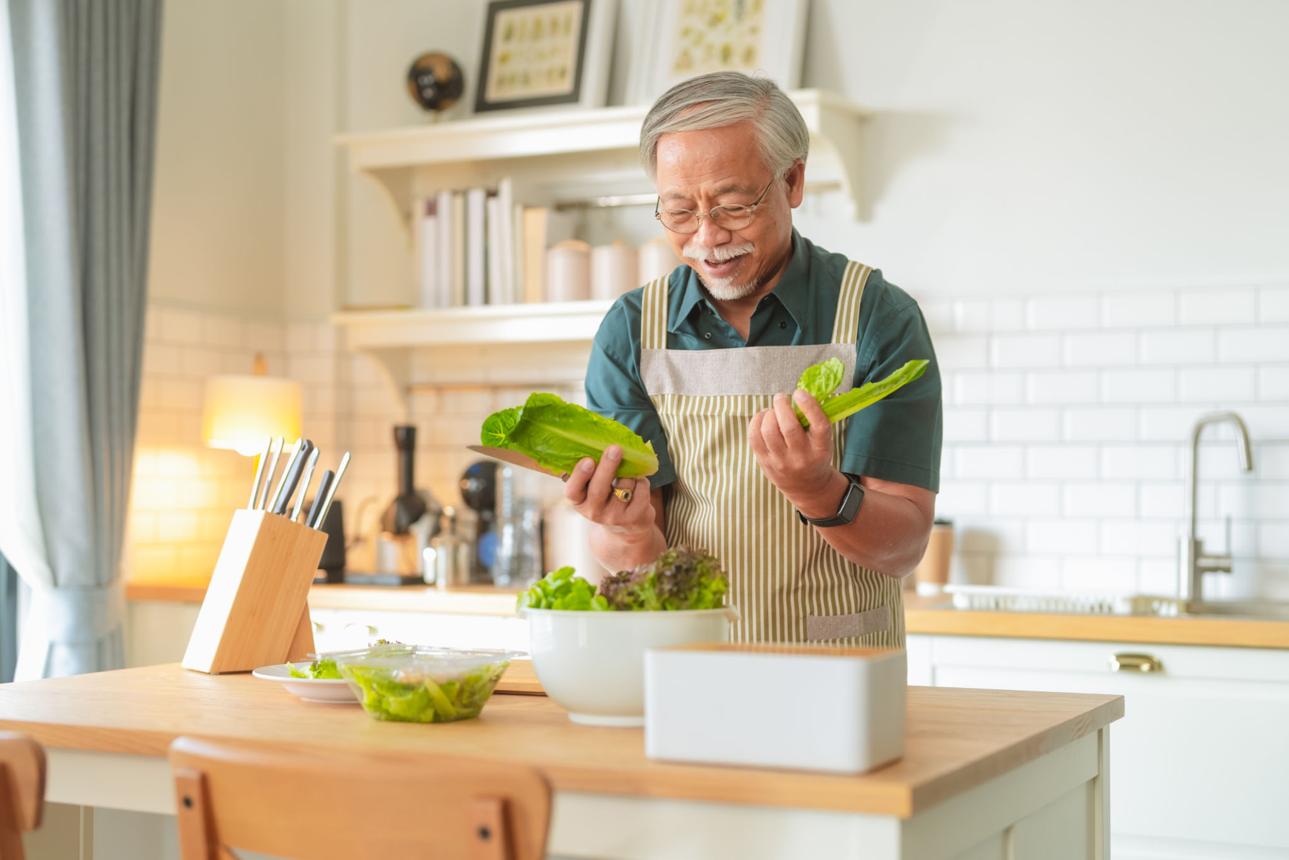 Elderly man happily preparing a meal at home